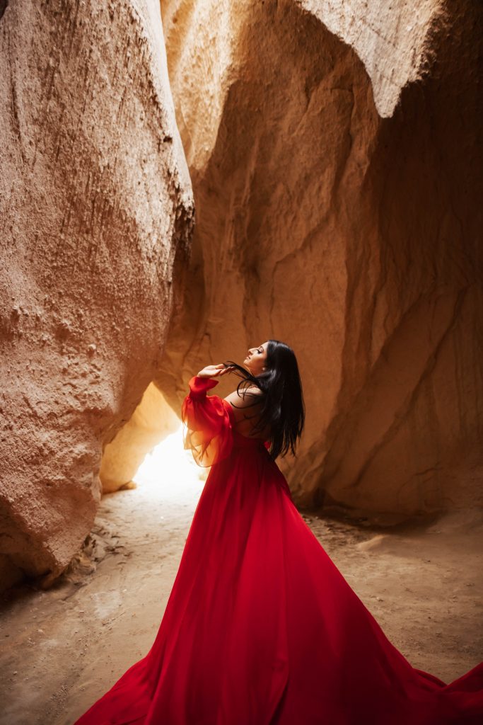 Woman in red dress inside cave in Cappadocia, Turkey during sunrise for a photoshoot