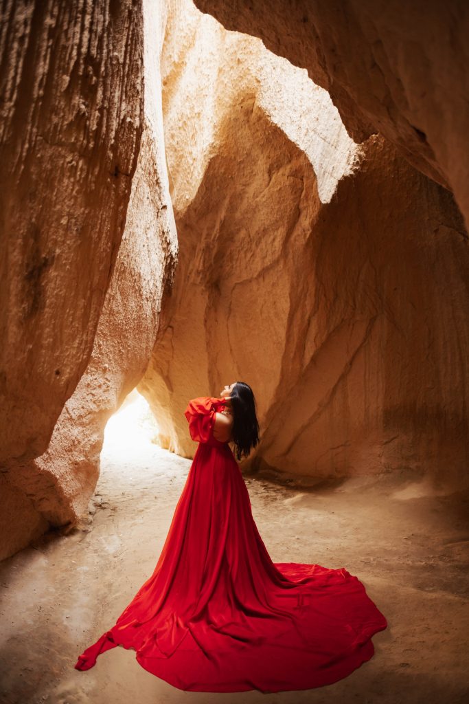 Woman in red dress inside cave in Cappadocia, Turkey during sunrise for a photoshoot