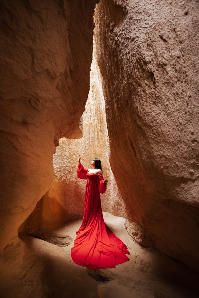Woman in red dress inside cave in Cappadocia, Turkey during sunrise for a photoshoot