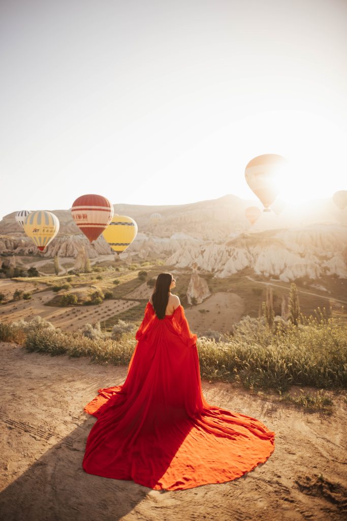 Red dress photoshoot in Cappadocia Turkey during sunrise with hot air balloons in the background