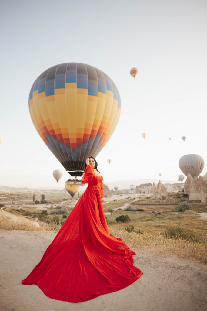 Red dress photoshoot in Cappadocia Turkey during sunrise with hot air balloons in the background