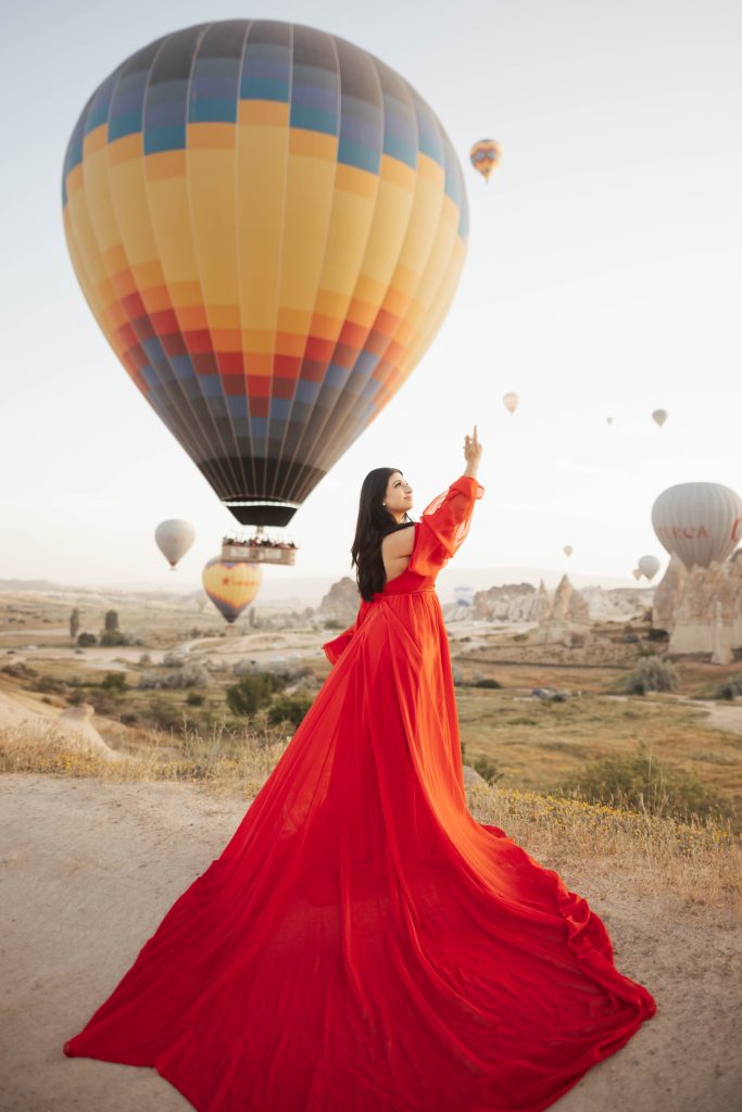 Red dress photoshoot in Cappadocia Turkey during sunrise with hot air balloons in the background