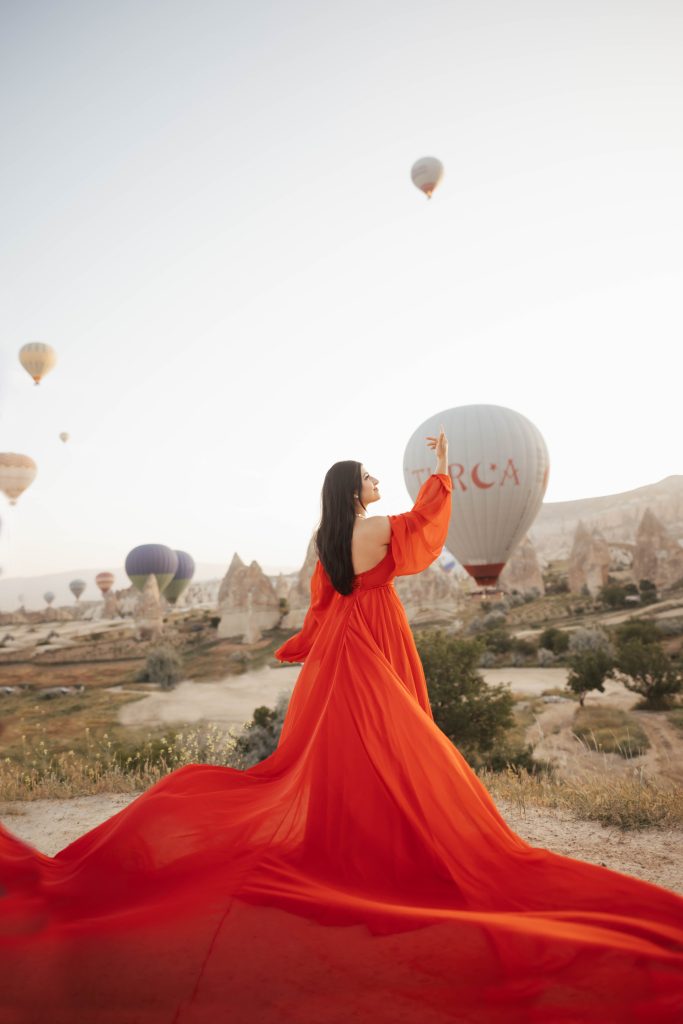 Red dress photoshoot in Cappadocia Turkey during sunrise with hot air balloons in the background