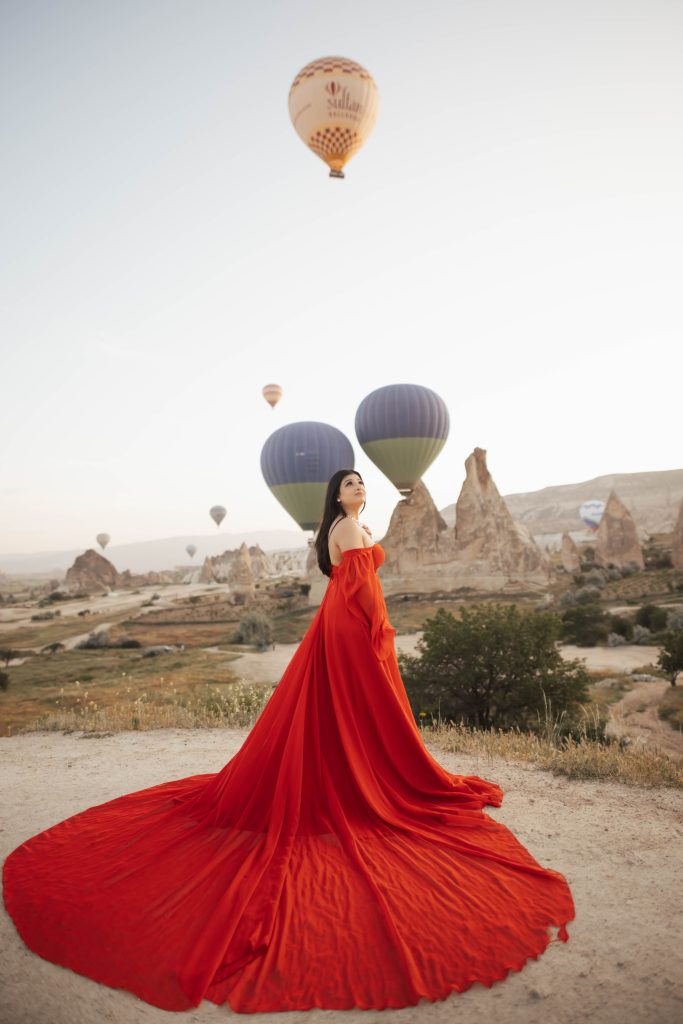 Red dress photoshoot in Cappadocia Turkey during sunrise with hot air balloons in the background