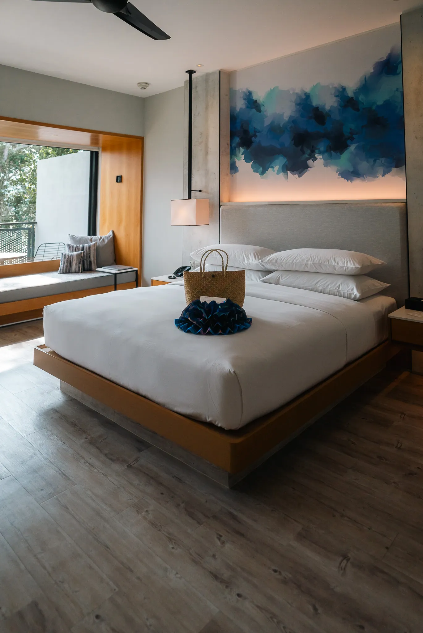 A king-size bed in a room at the Perhentian Marriott Resort & Spa, neatly made with white linens, a complimentary woven bag,