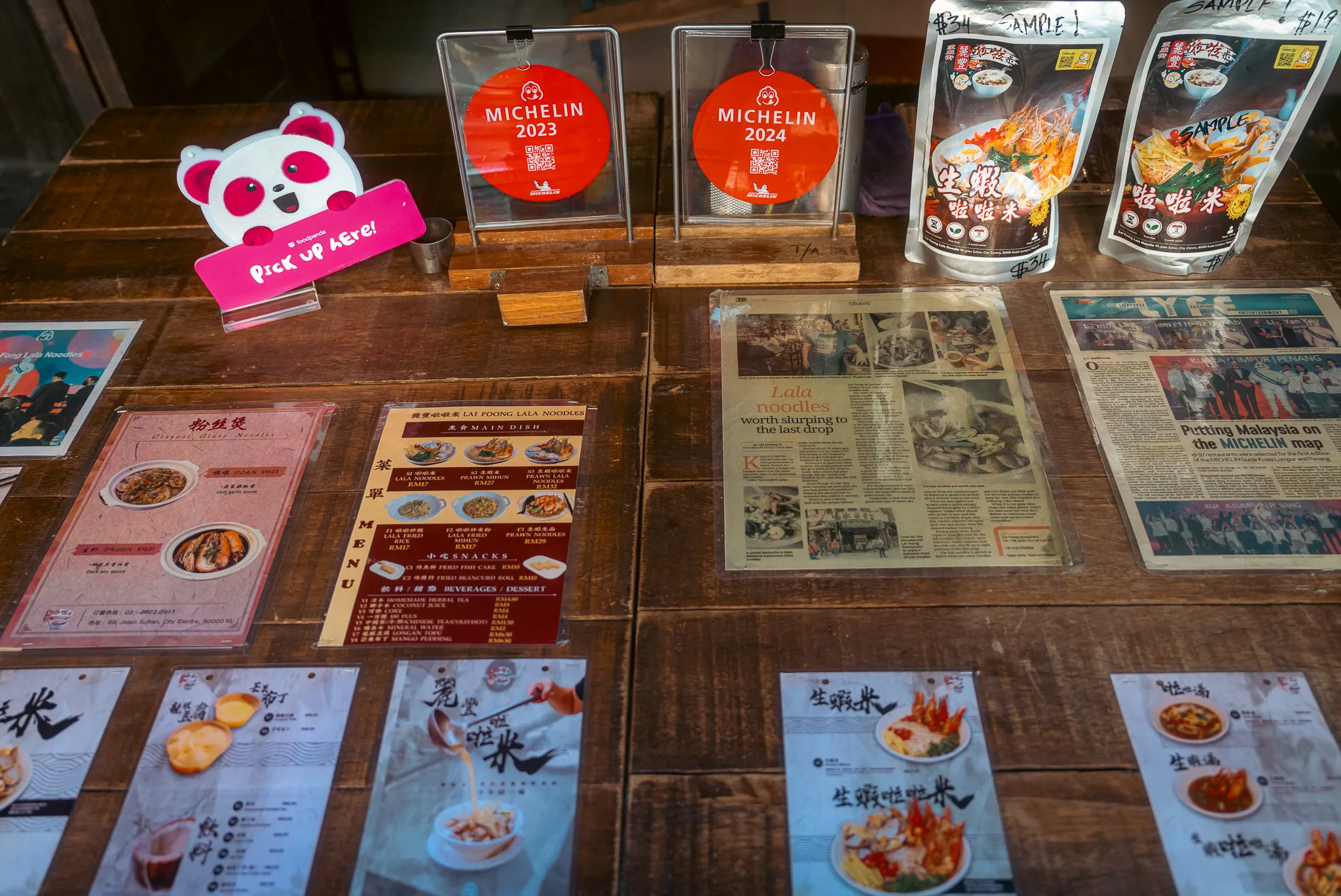 Display table at Lai Foong Lala Noodles, Kuala Lumpur, featuring Michelin Bib Gourmand awards and press clippings